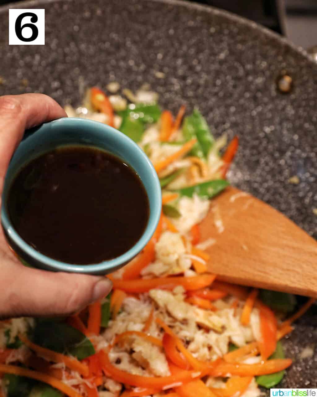hand holding sauce over wok full of vegetables to make crab pancit.