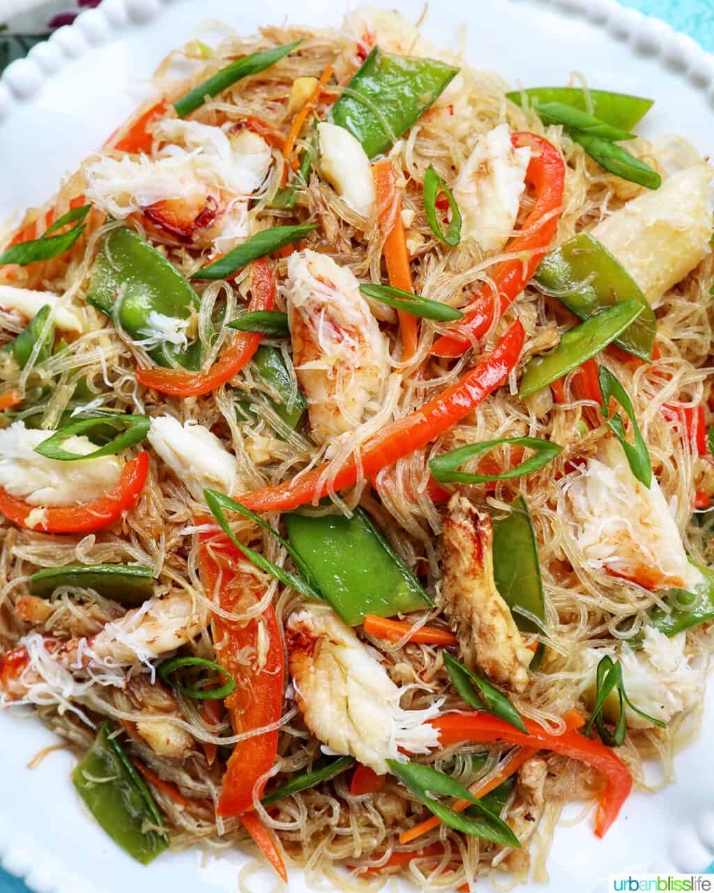 crab pancit filipino noodles in a large bowl, with slices veggies and chunks of crab meat.