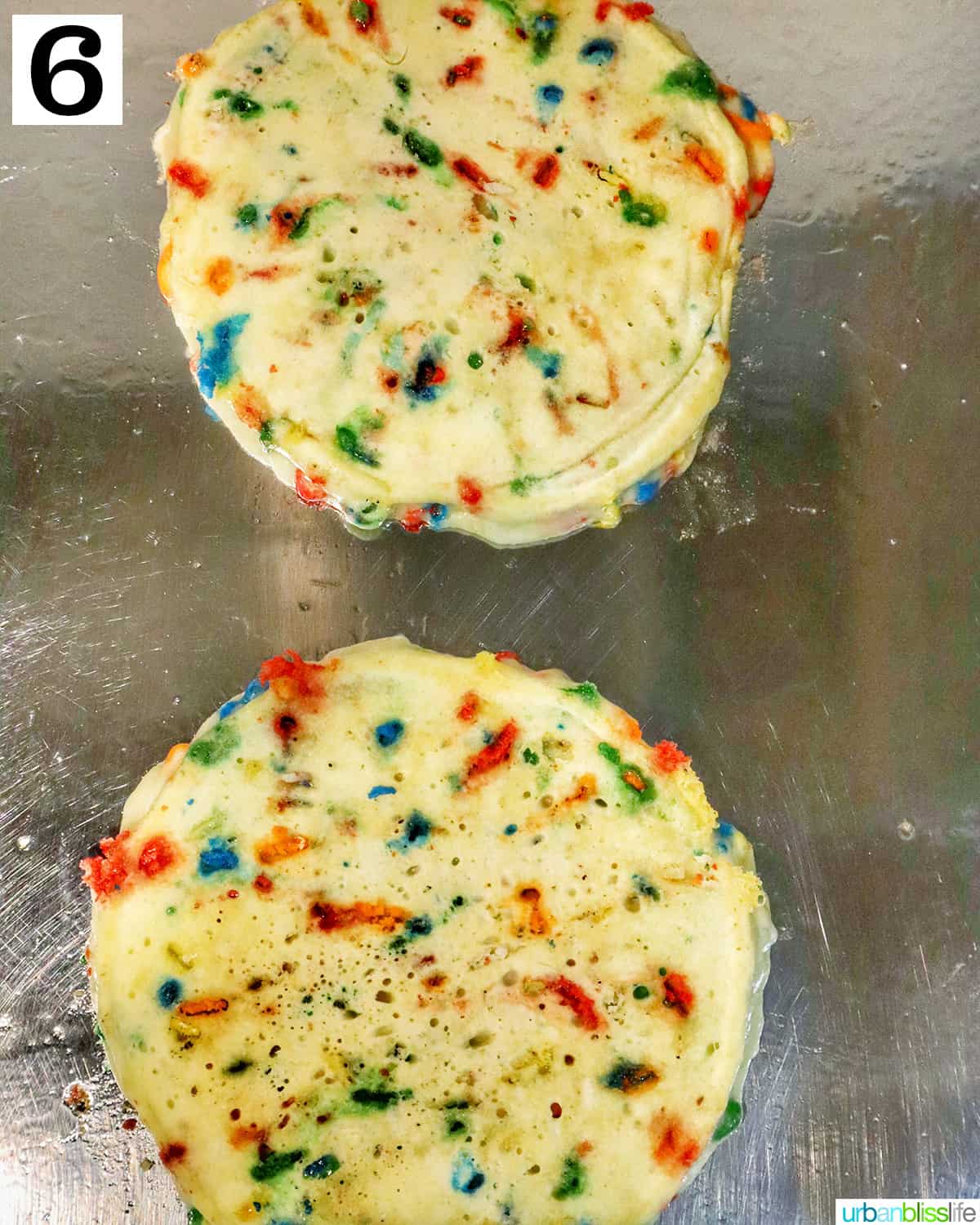 two funfetti pancakes cooking on a stovetop griddle.