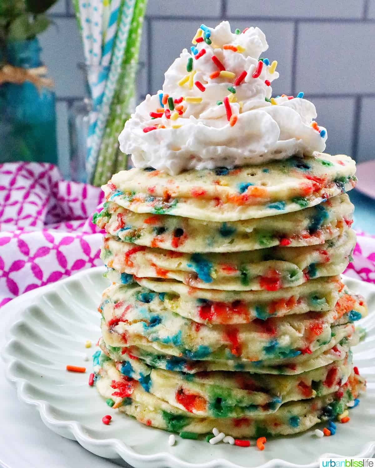 stack of funfetti pancakes with whipped cream and extra sprinkles on a light green plate.