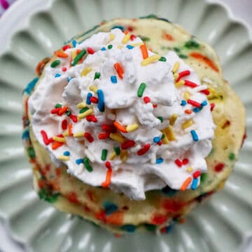 stack of funfetti pancakes with whipped cream and extra sprinkles on a light green plate.
