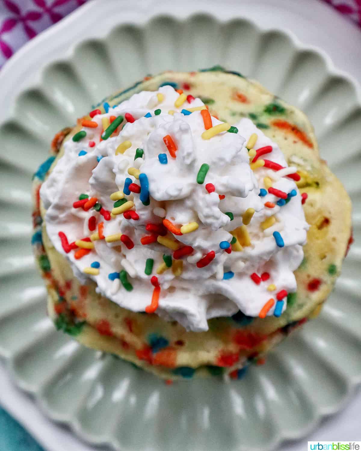 stack of funfetti pancakes with whipped cream and extra sprinkles on a light green plate.
