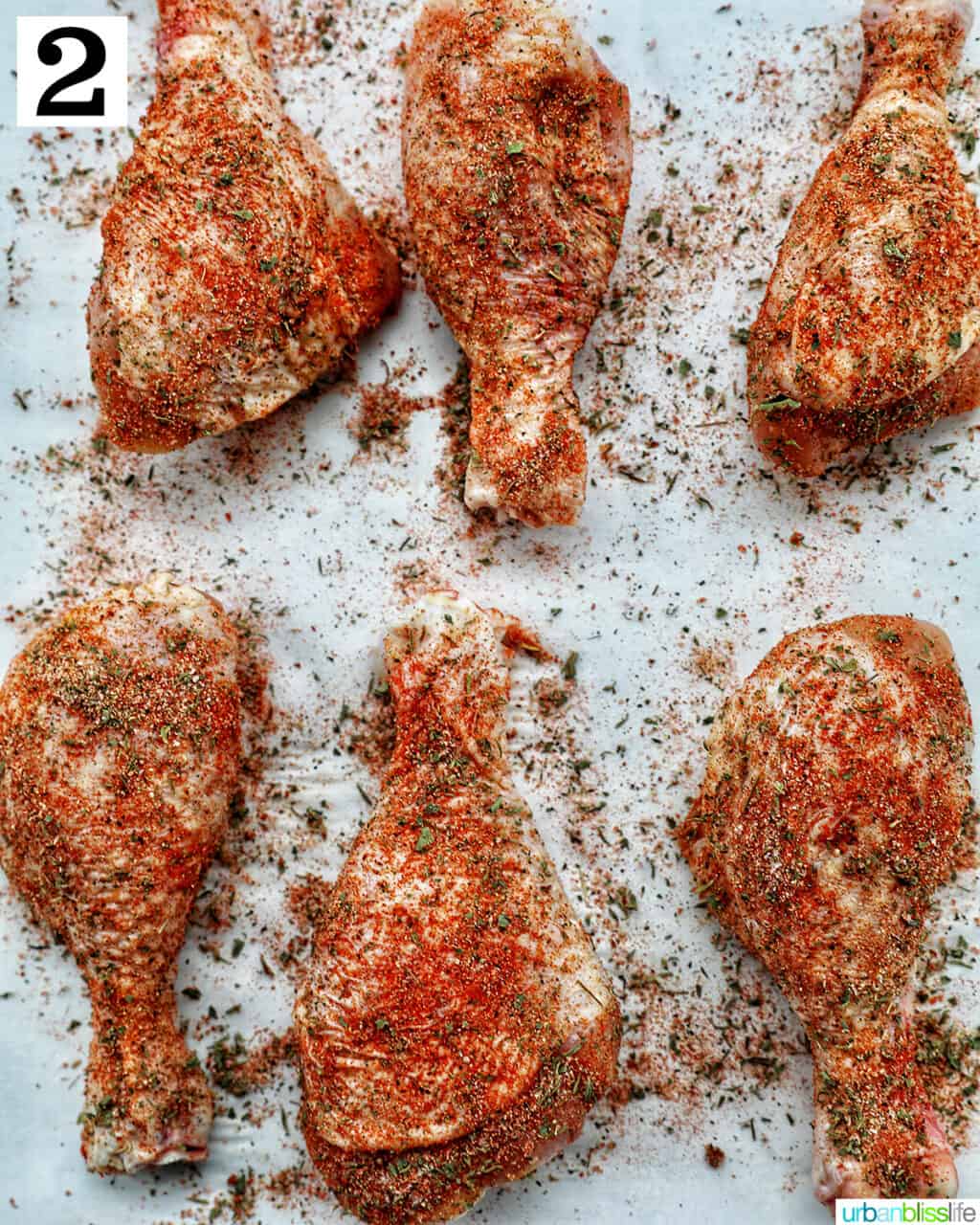 six chicken drumsticks seasoned on a parchment paper.
