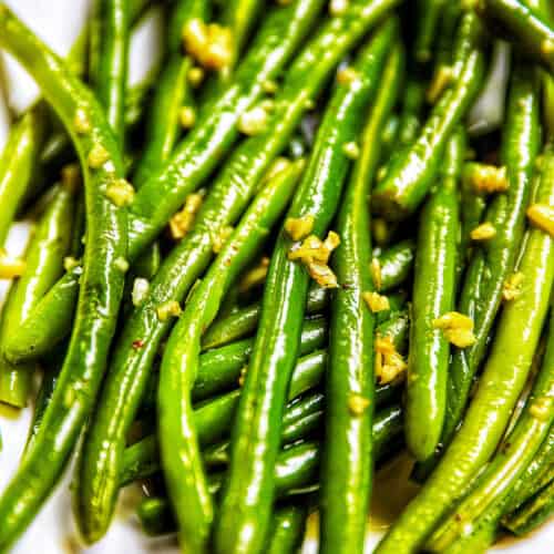 close up of green beans with garlic in a white bowl.