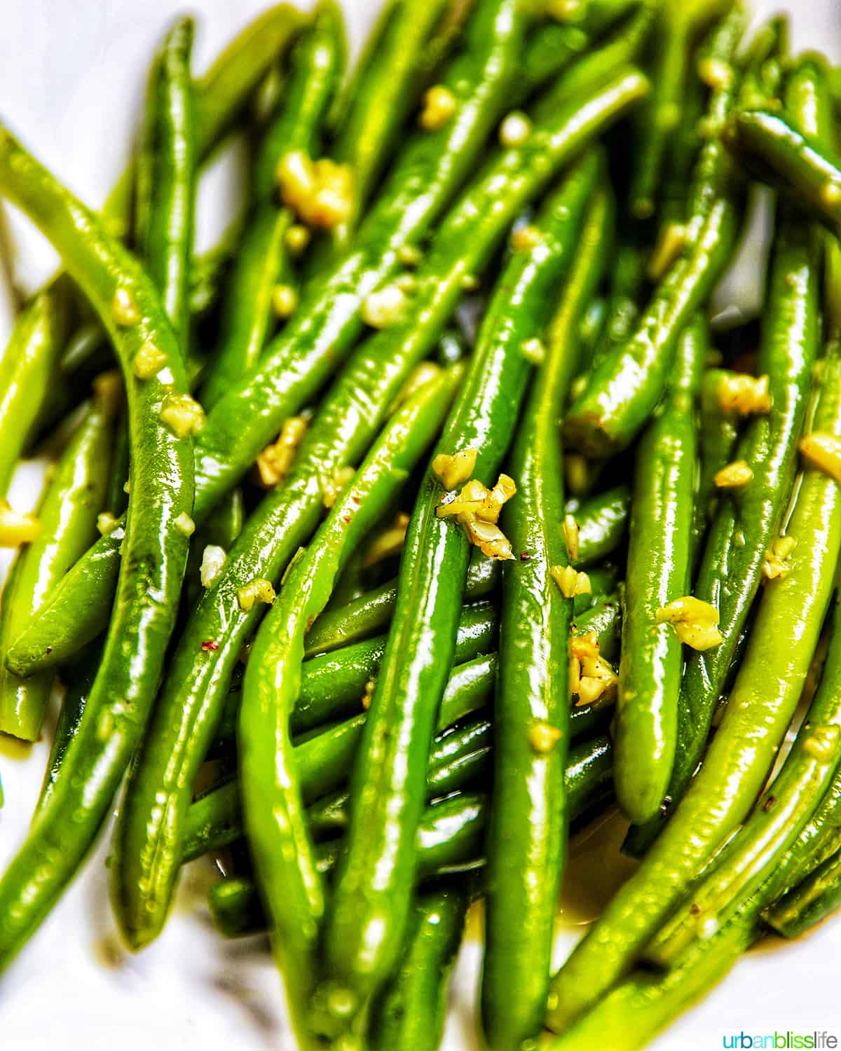 close up of green beans with garlic in a white bowl.