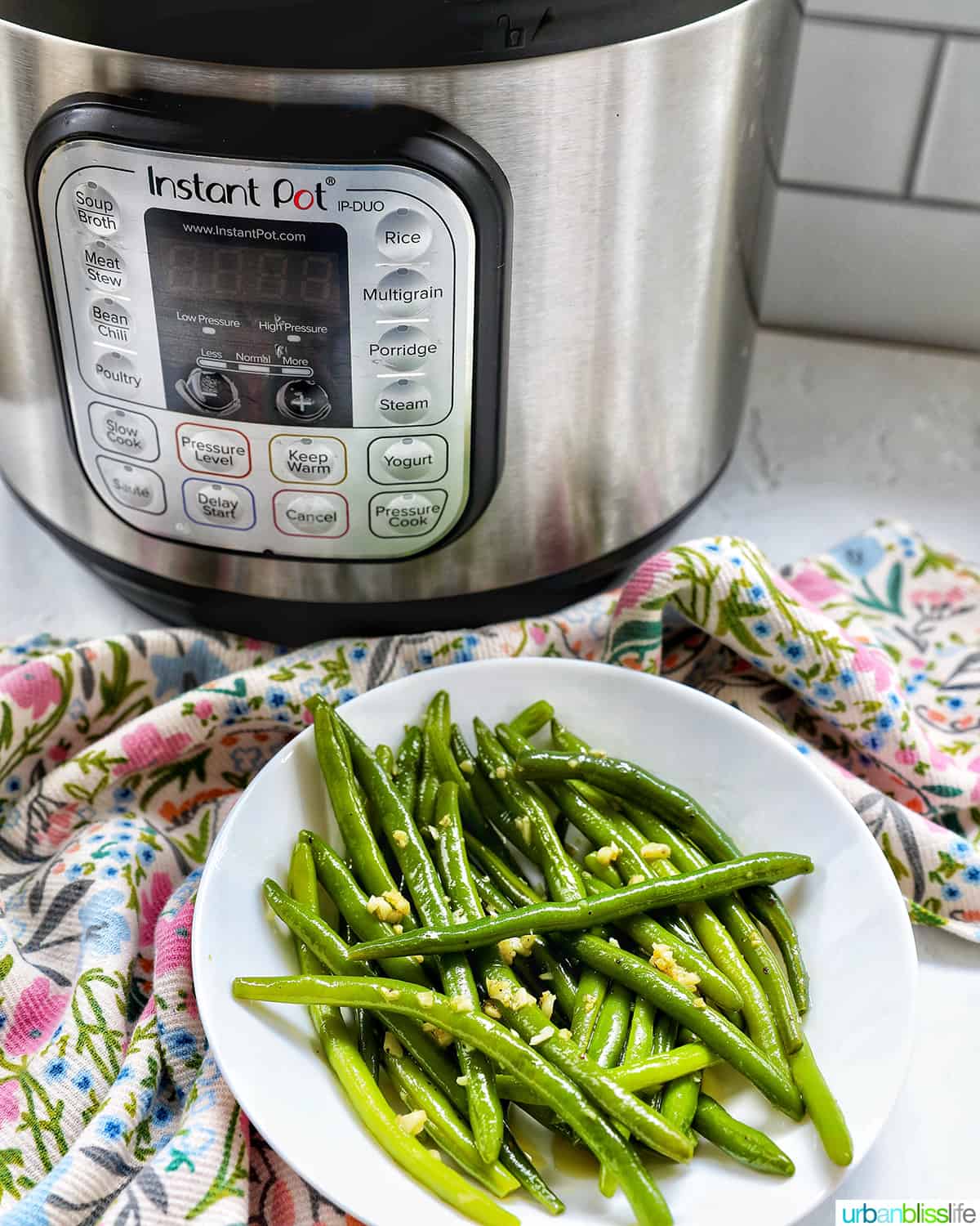 green beans with garlic in a white bowl in front of an Instant Pot pressure cooker.
