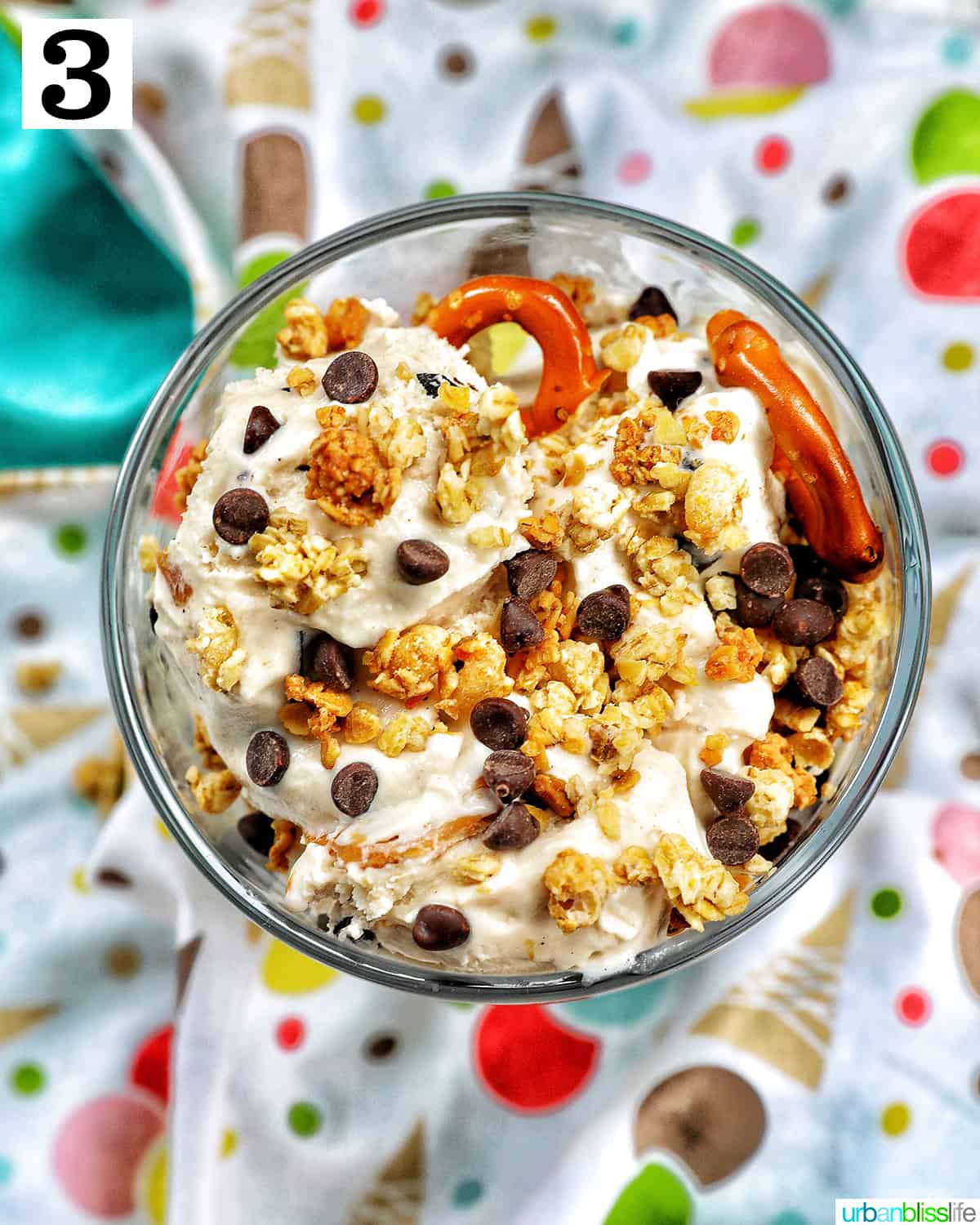 ice cream parfait topped with granola, mini chocolate chips on a colorful kitchen towel.
