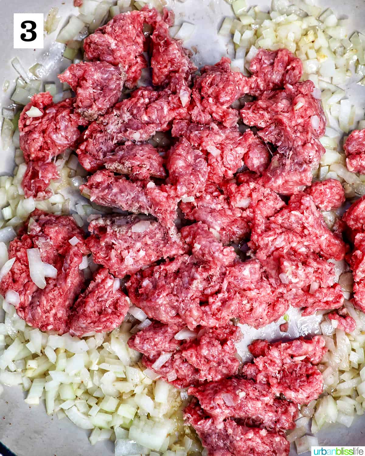 ground beef added to sautéed onions and garlic in a pan.