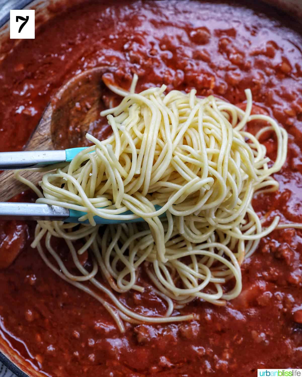 tongs adding spaghetti to Filipino spaghetti sauce in a pan.