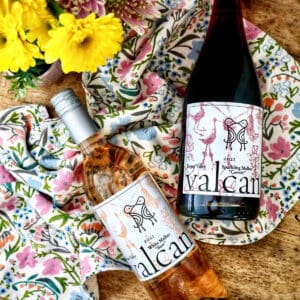Valcan Cellars bottle of White Malbec and Sparkling Malbec on spring towel on a wine barrel with spring flowers.
