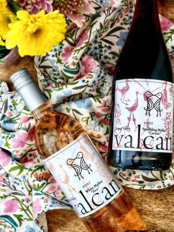 Valcan Cellars bottle of White Malbec and Sparkling Malbec on spring towel on a wine barrel with spring flowers.