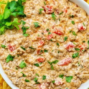 taco dip with ground beef, tomatoes, and cilantro in a large white bowl.