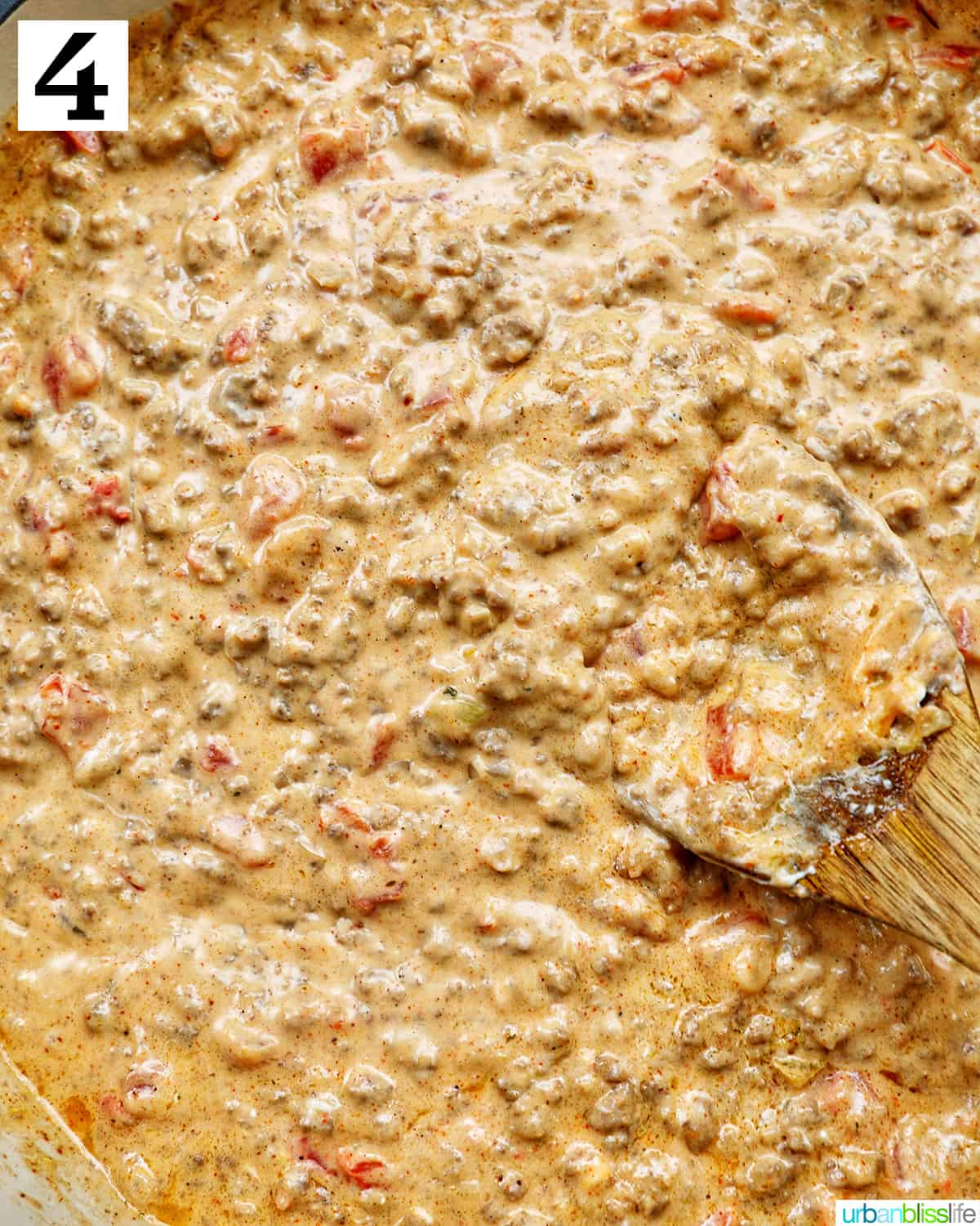 cheesy taco dip with ground beef cooking in a pan with a wooden spoon.