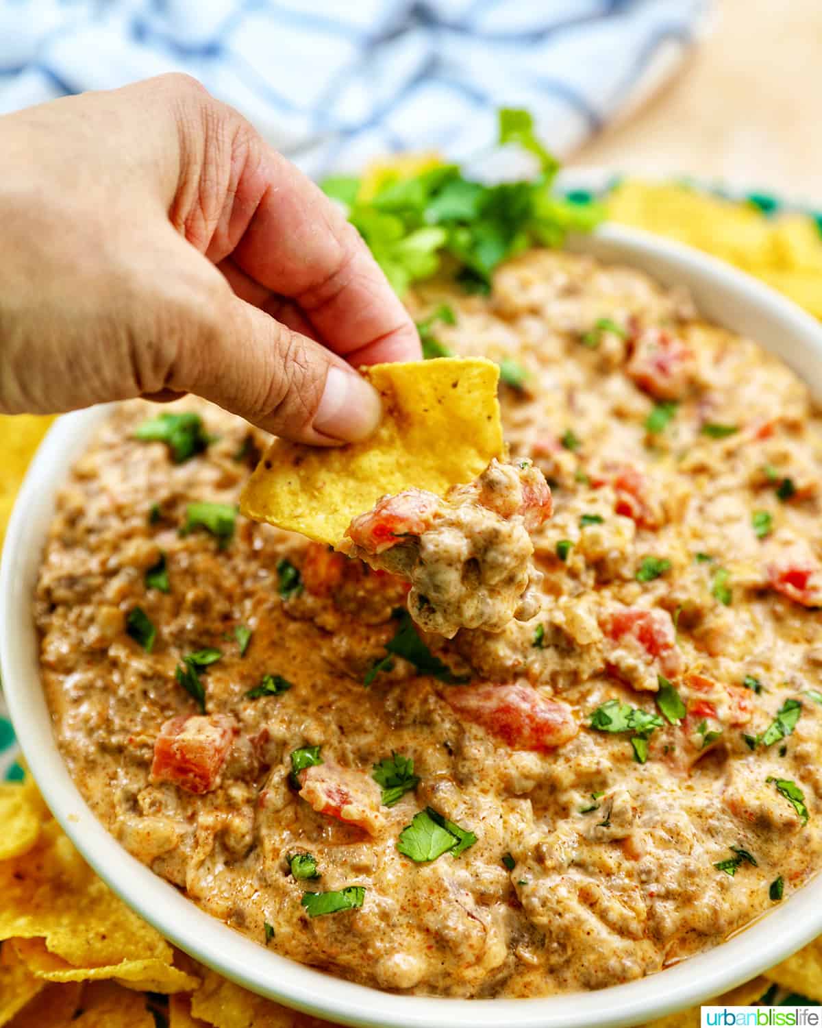 taco dip in a large white bowl with a hand dipping a chip into the dip