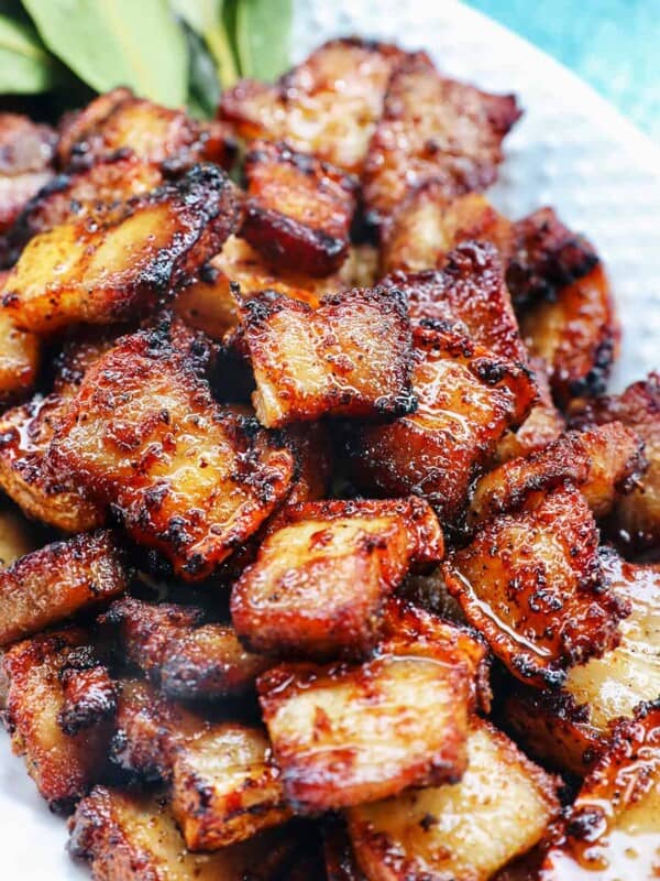 pile of air fryer pork belly bites on a white serving platter with bay leaves on a blue background.