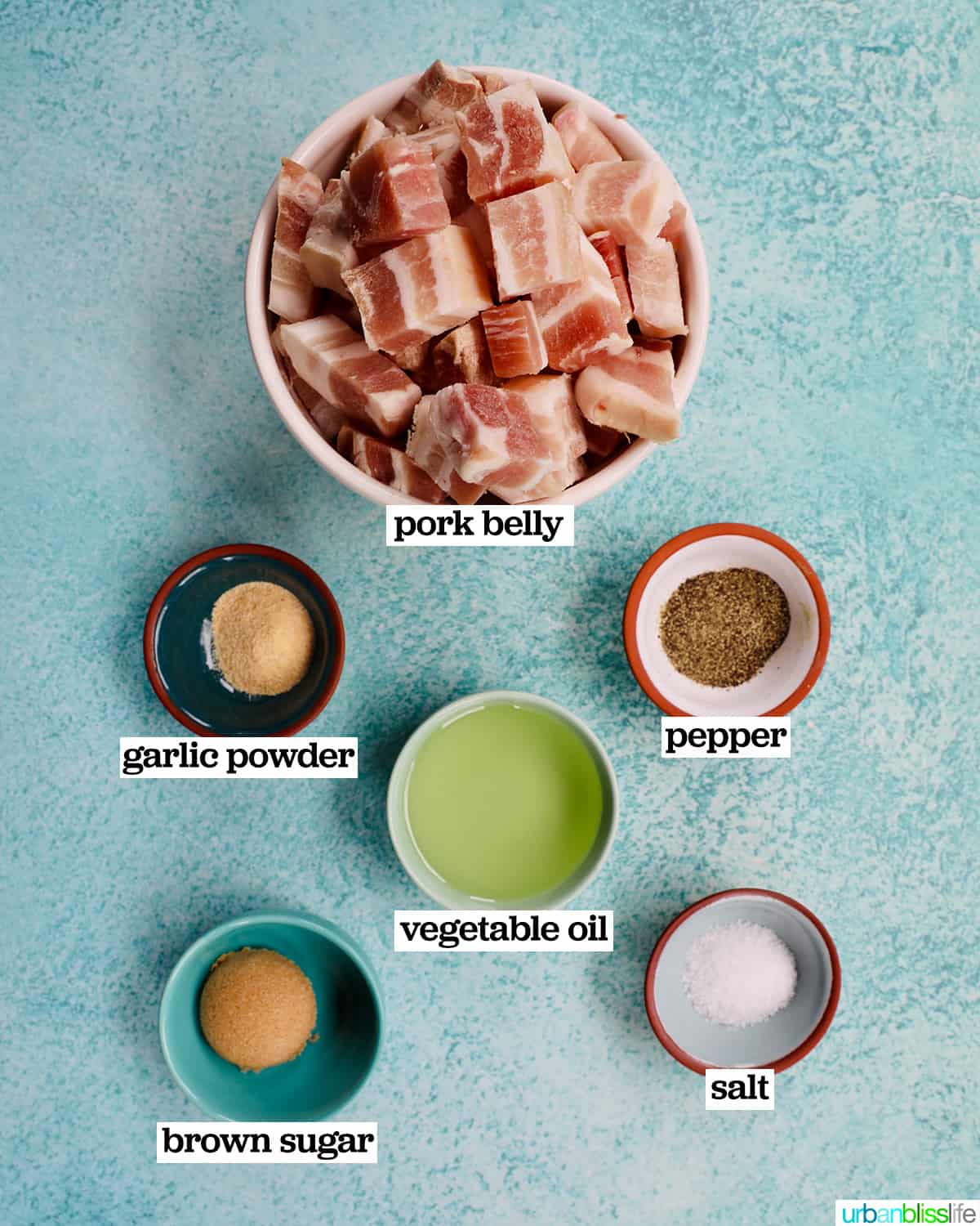 bowls of ingredients to make air fryer pork belly bites on a blue background.