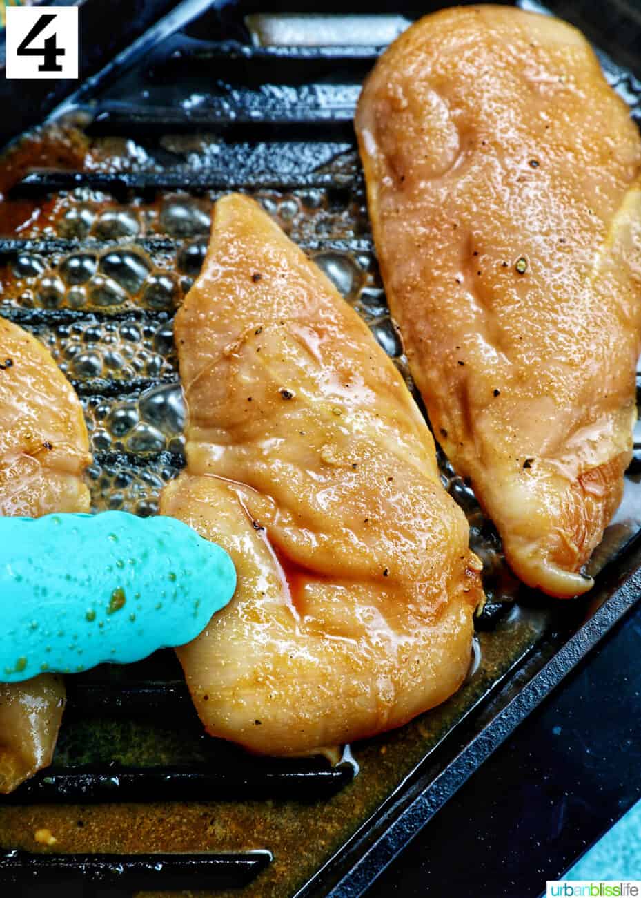 blue tongs flipping over a chicken breast next to other chicken breasts on a grill.