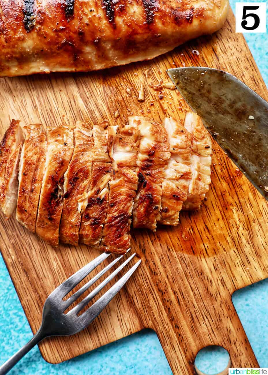fork and knife slicing grilled teriyaki chicken breasts on a wooden board with blue background.