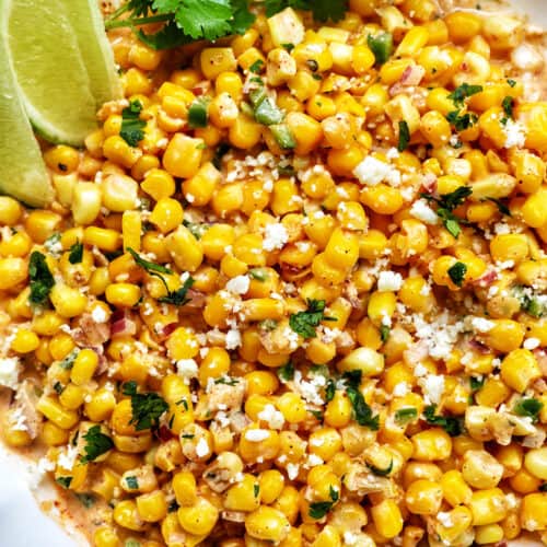 big bowl of elote dip (Mexican corn dip) with side of lime wedges and cilantro.