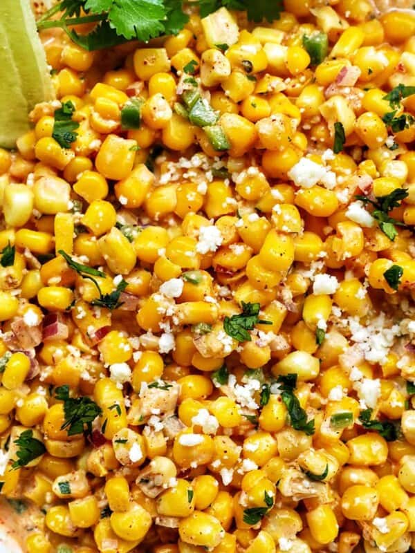 big bowl of elote dip (Mexican corn dip) with side of lime wedges and cilantro.