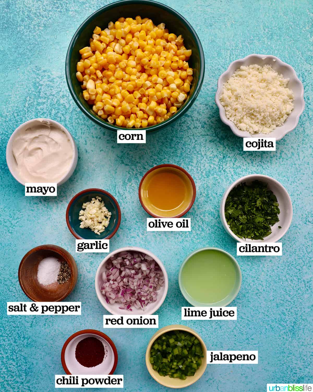 bowls of ingredients to make elote dip on a bright blue background.