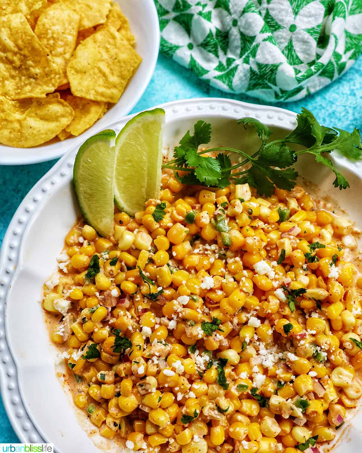 big bowl of elote dip (Mexican corn dip) with side of lime wedges and cilantro.