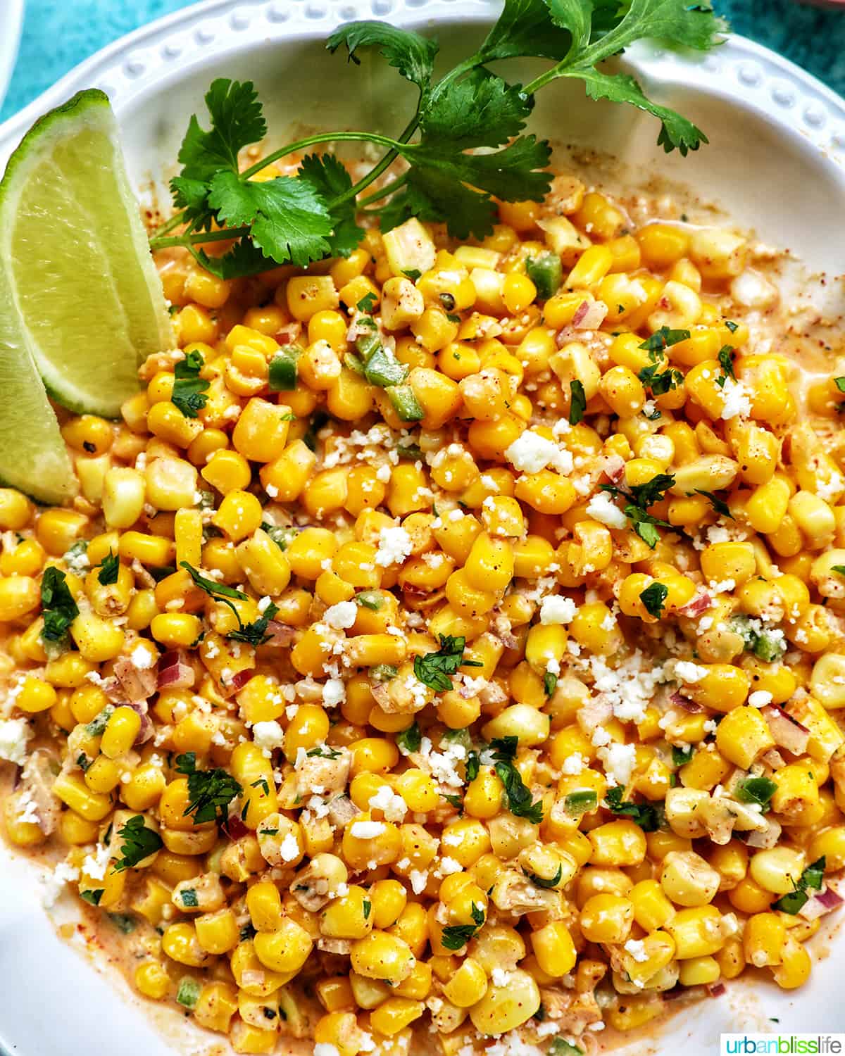 big bowl of elote dip (Mexican corn dip) with side of lime wedges and cilantro.