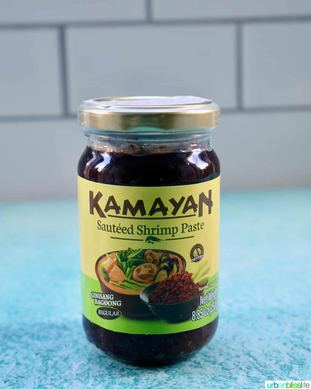 bottle of Kamayan shrimp paste (bagoong) on a blue table with white tile background.
