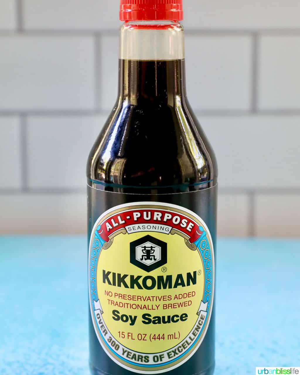 bottle of Kikkoman Soy Sauce on a blue table with white tile background.