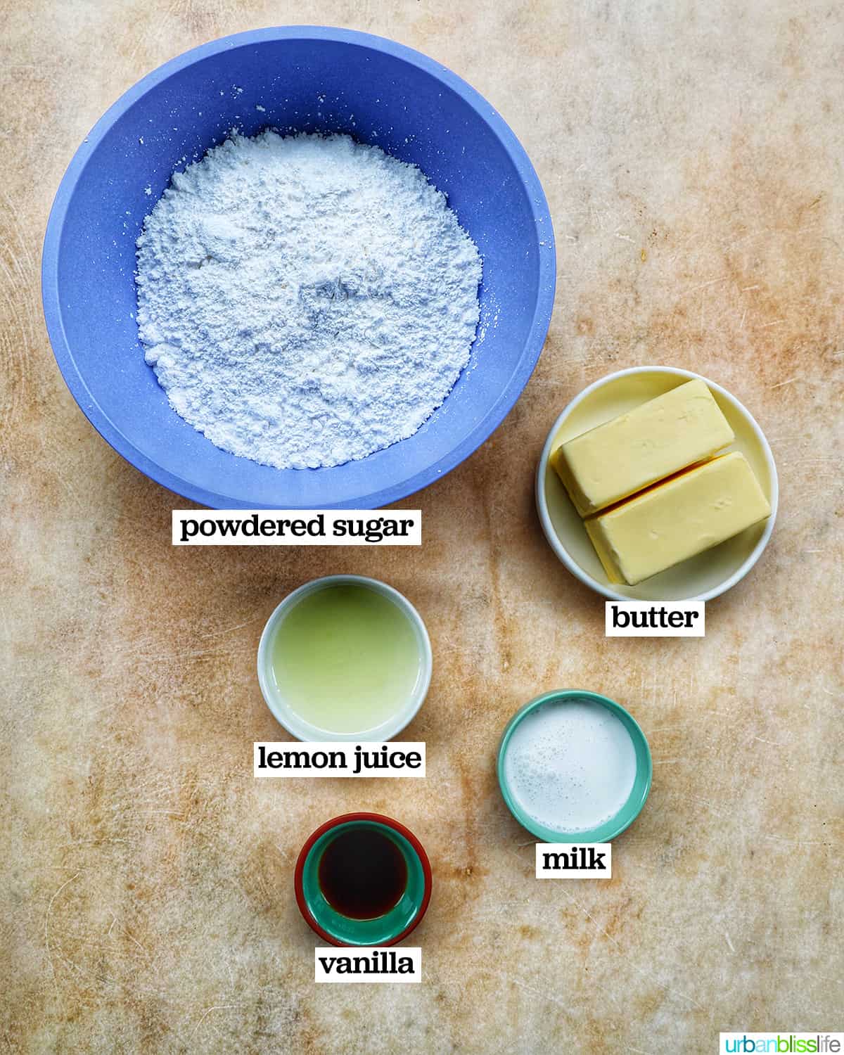 bowls of ingredients to make lemon buttercream frosting on a yellow background.