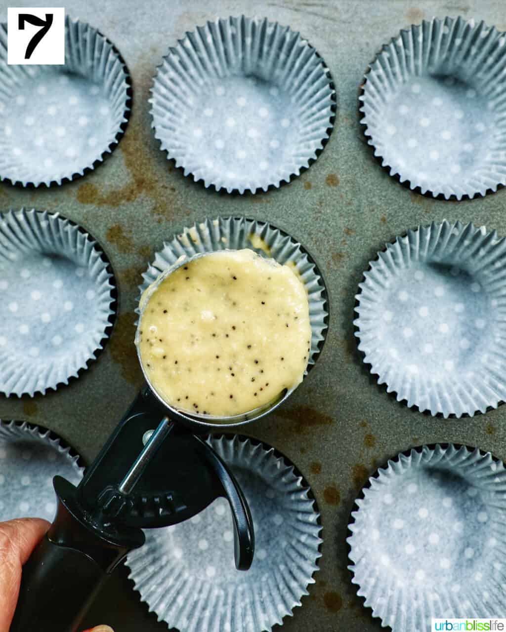 large cookie scoop with cupcake batter over a muffin tin lined with cupcake liners.