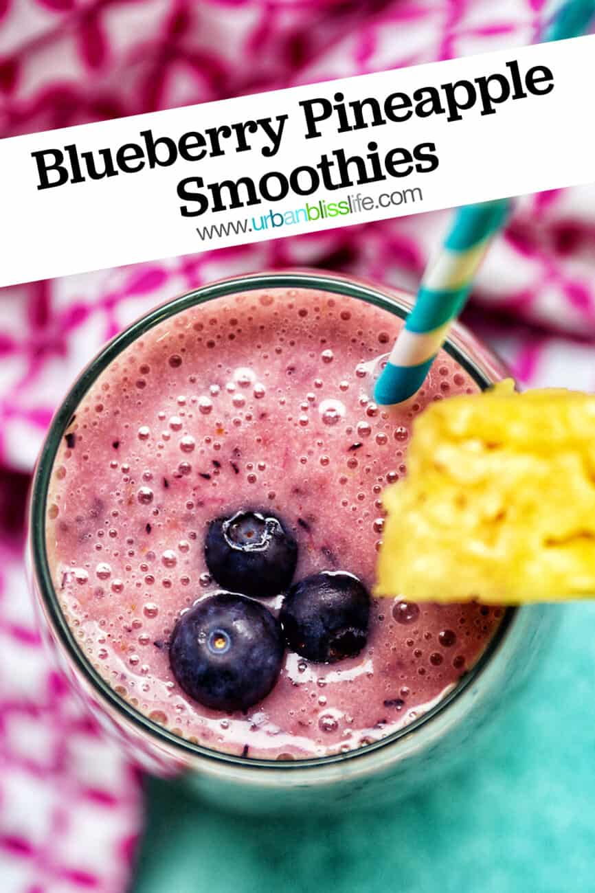glass of Blueberry Pineapple Smoothie with pineapple wedge garnish, blue and white stripe straw, and pink and white napkin.