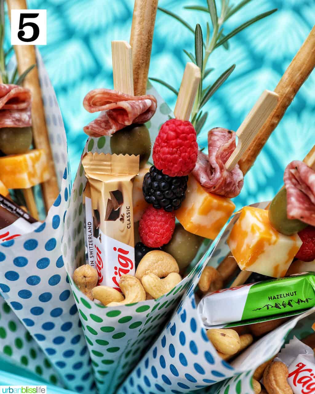 Charcuterie cones with fruit, cheeses, breadsticks, nuts, chocolate, herbs in paper cones.