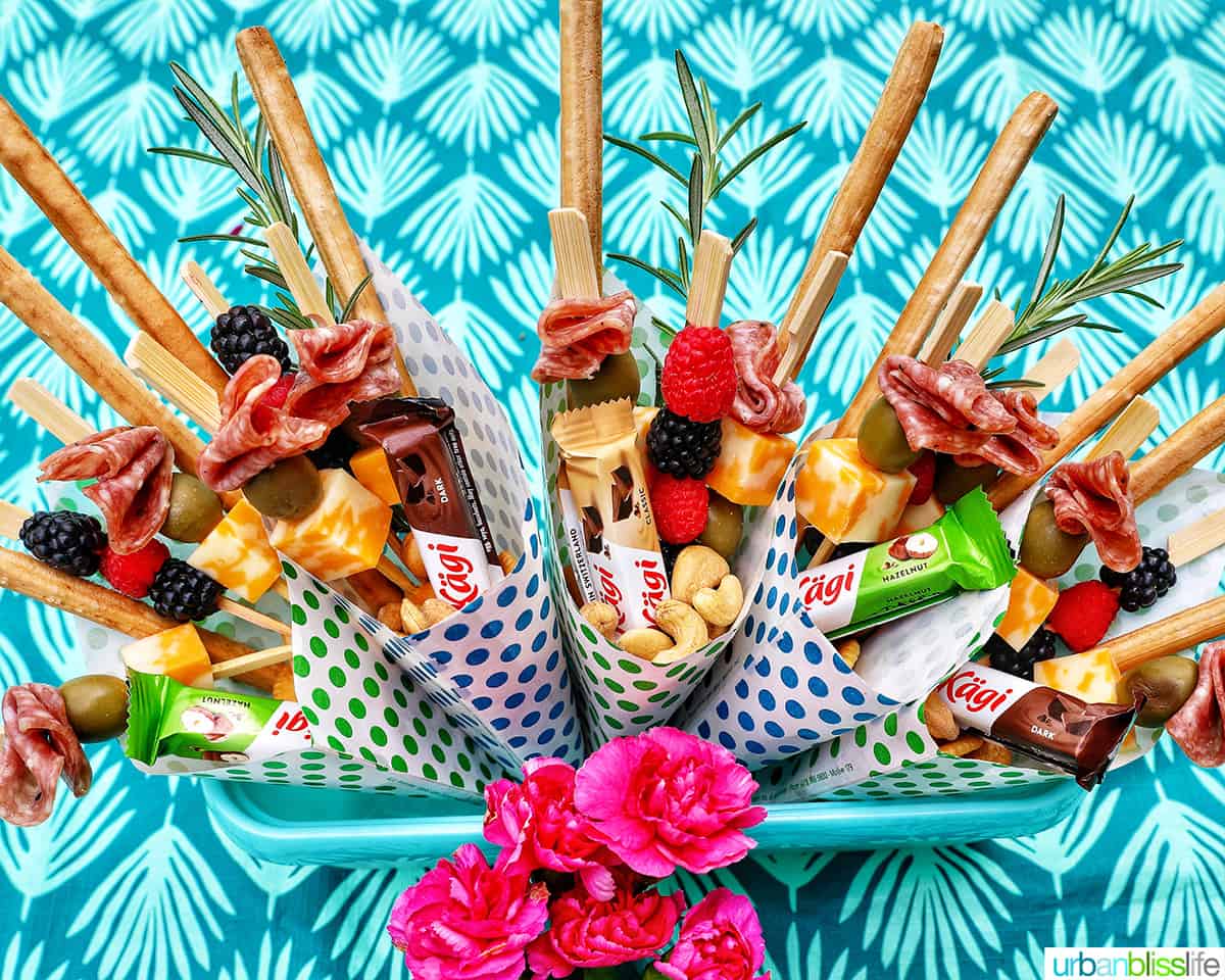 Charcuterie cones with fruit, cheeses, breadsticks, nuts, chocolate, herbs in paper cones.