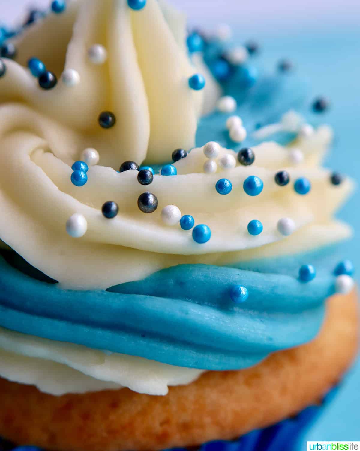 swirls of white and blue vanilla buttercream frosting with white and blue sprinkles on a vanilla cupcake.