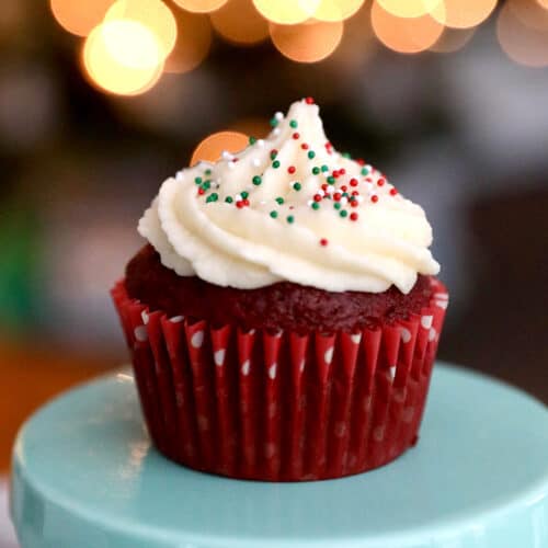 vanilla buttercream frosting on a red velvet cupcake with bokeh twinkle lights in the background.