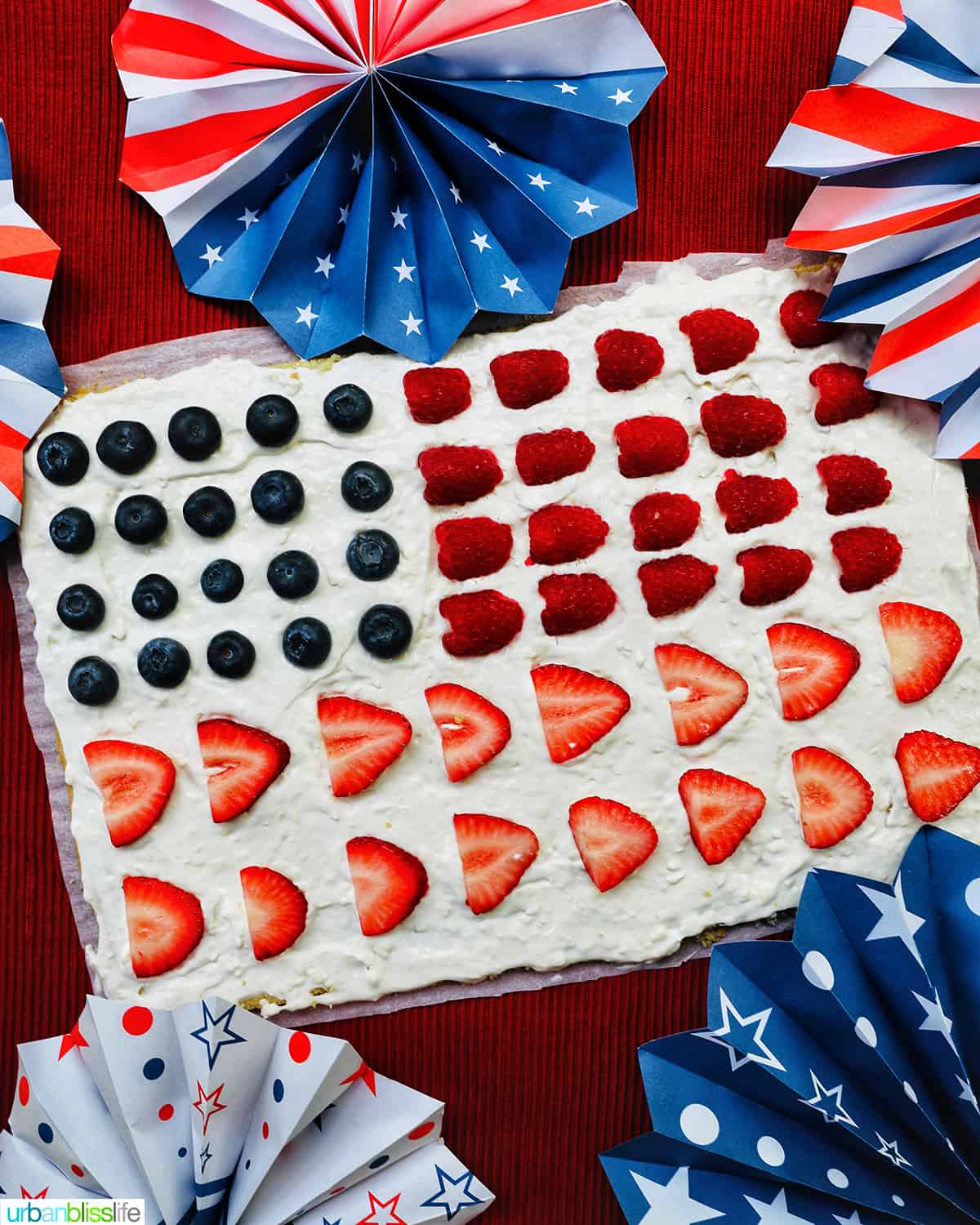 4th of July Fruit Pizza with blueberries, strawberries, raspberries surrounded by red, white, and blue decorations.