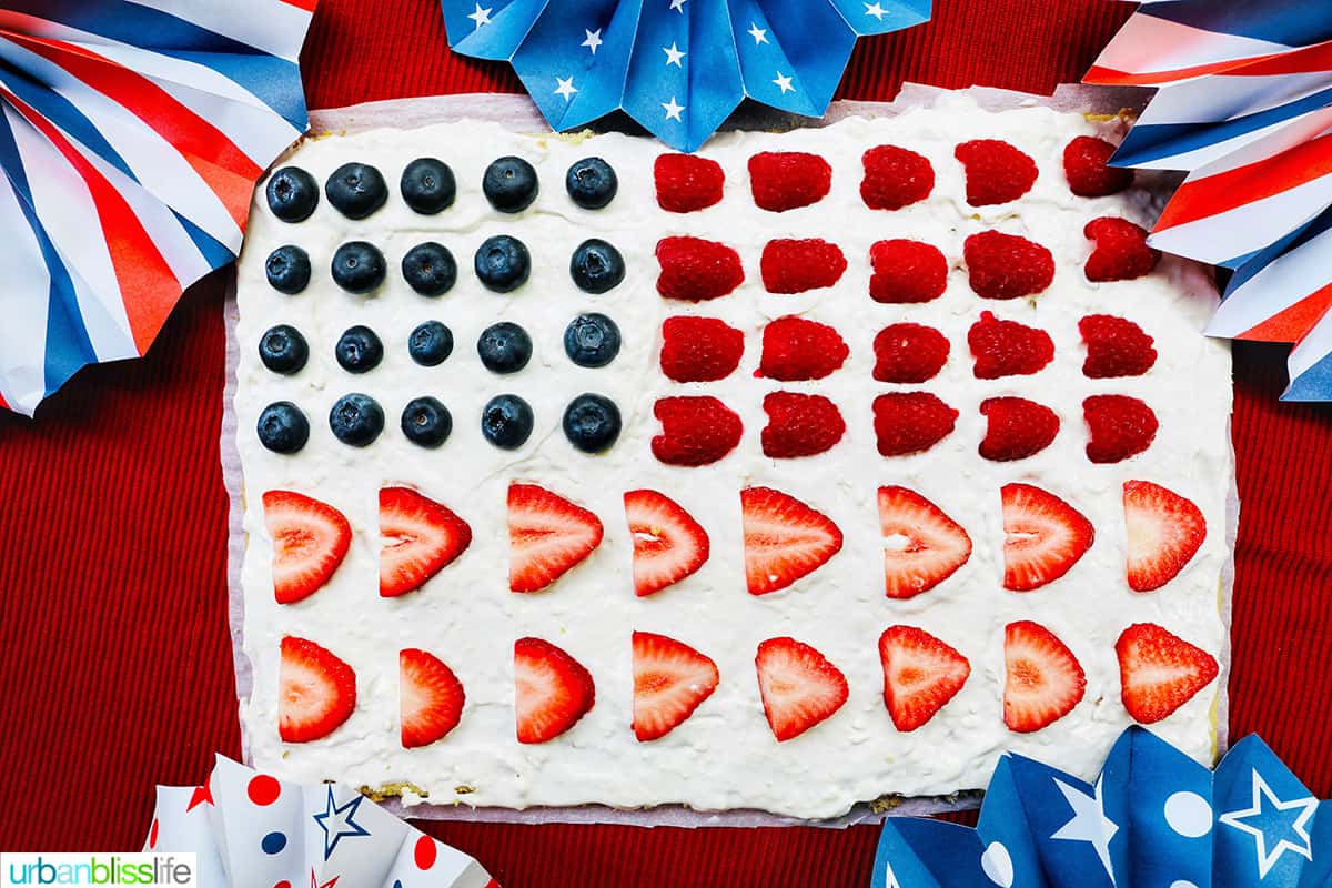 4th of July Fruit Pizza with blueberries, strawberries, raspberries surrounded by red, white, and blue decorations.