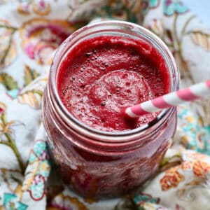 mason jar with red beet juice, a pink and white straw, on a colorful napkin.