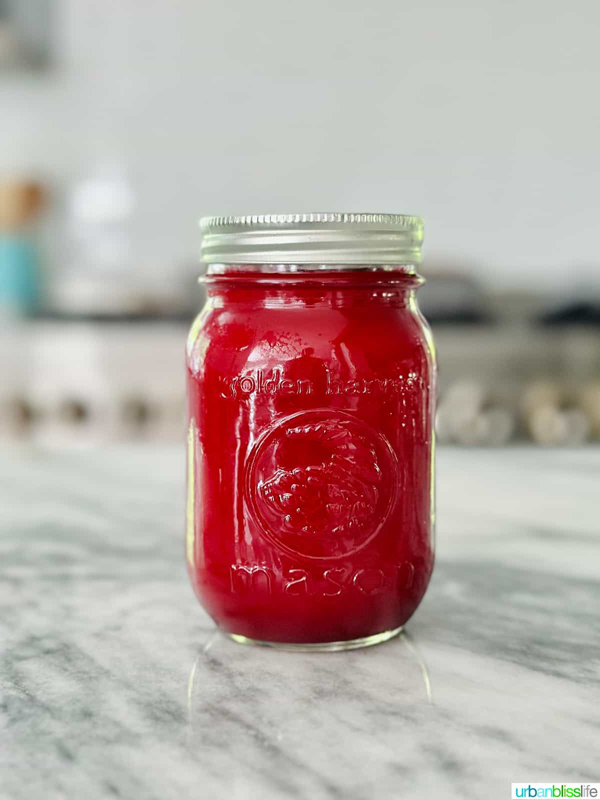 mason jar full of vibrant red beet juice on a marble countertop.