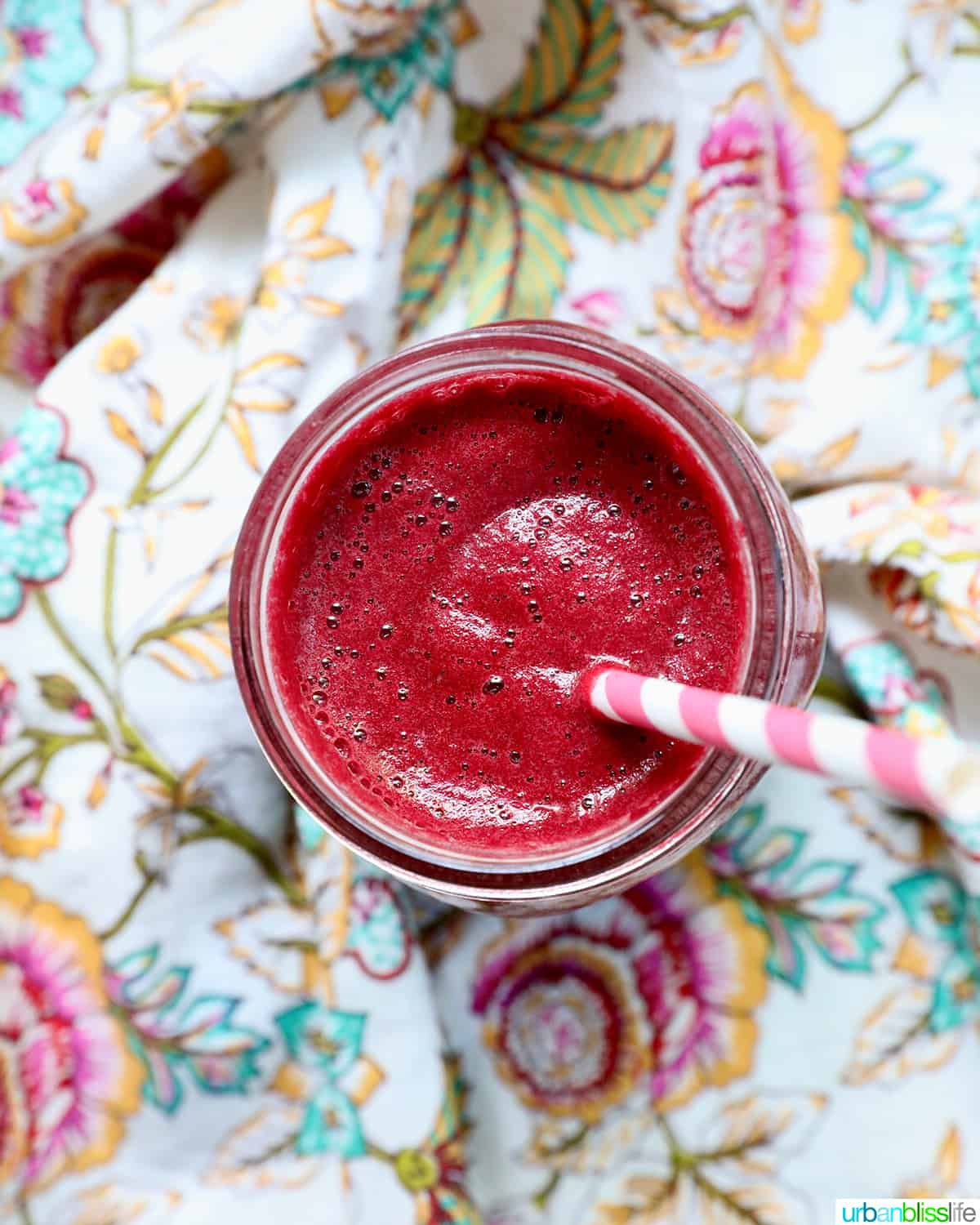 mason jar with red beet juice, a pink and white straw, on a colorful napkin.