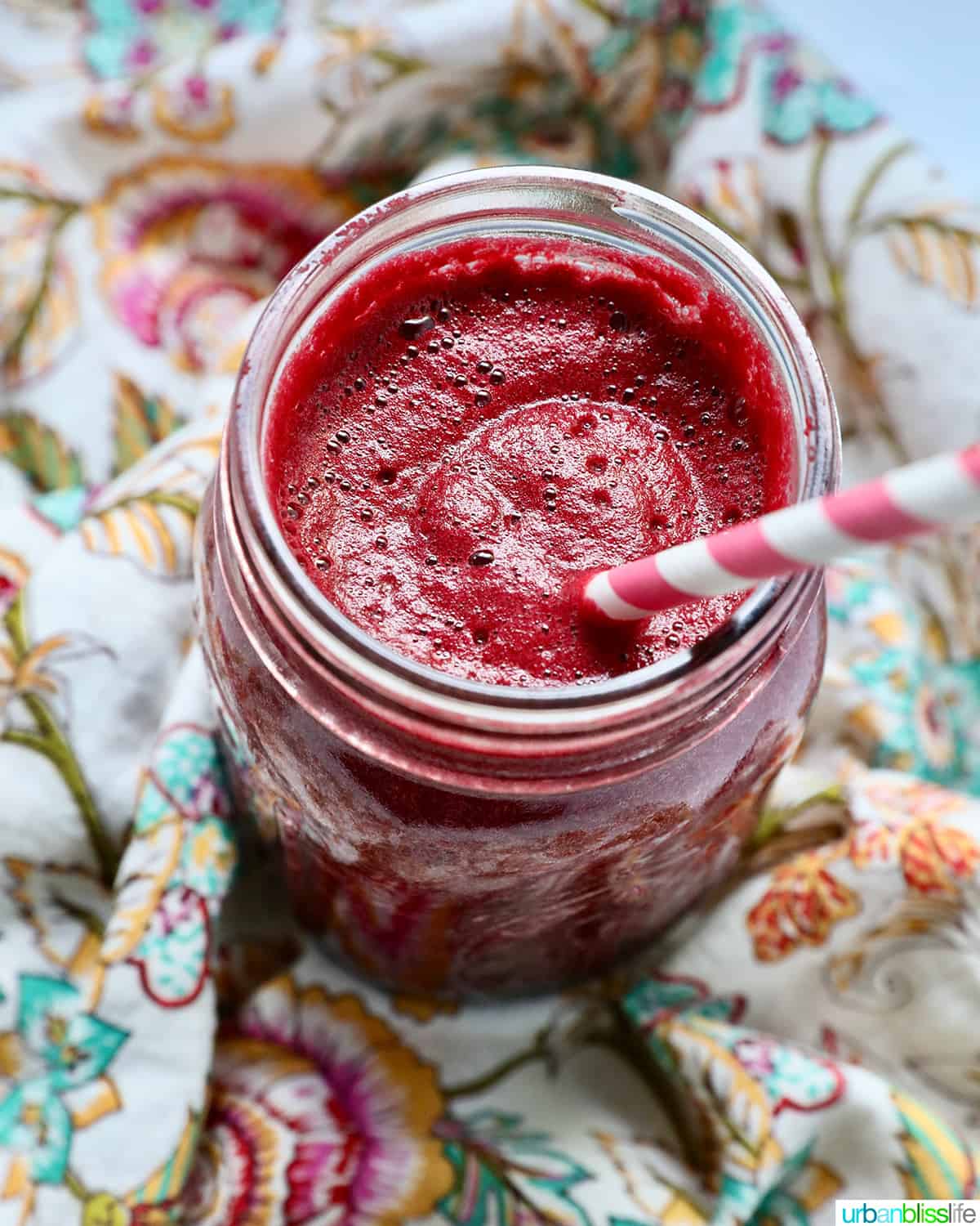 mason jar with red beet juice, a pink and white straw, on a colorful napkin.
