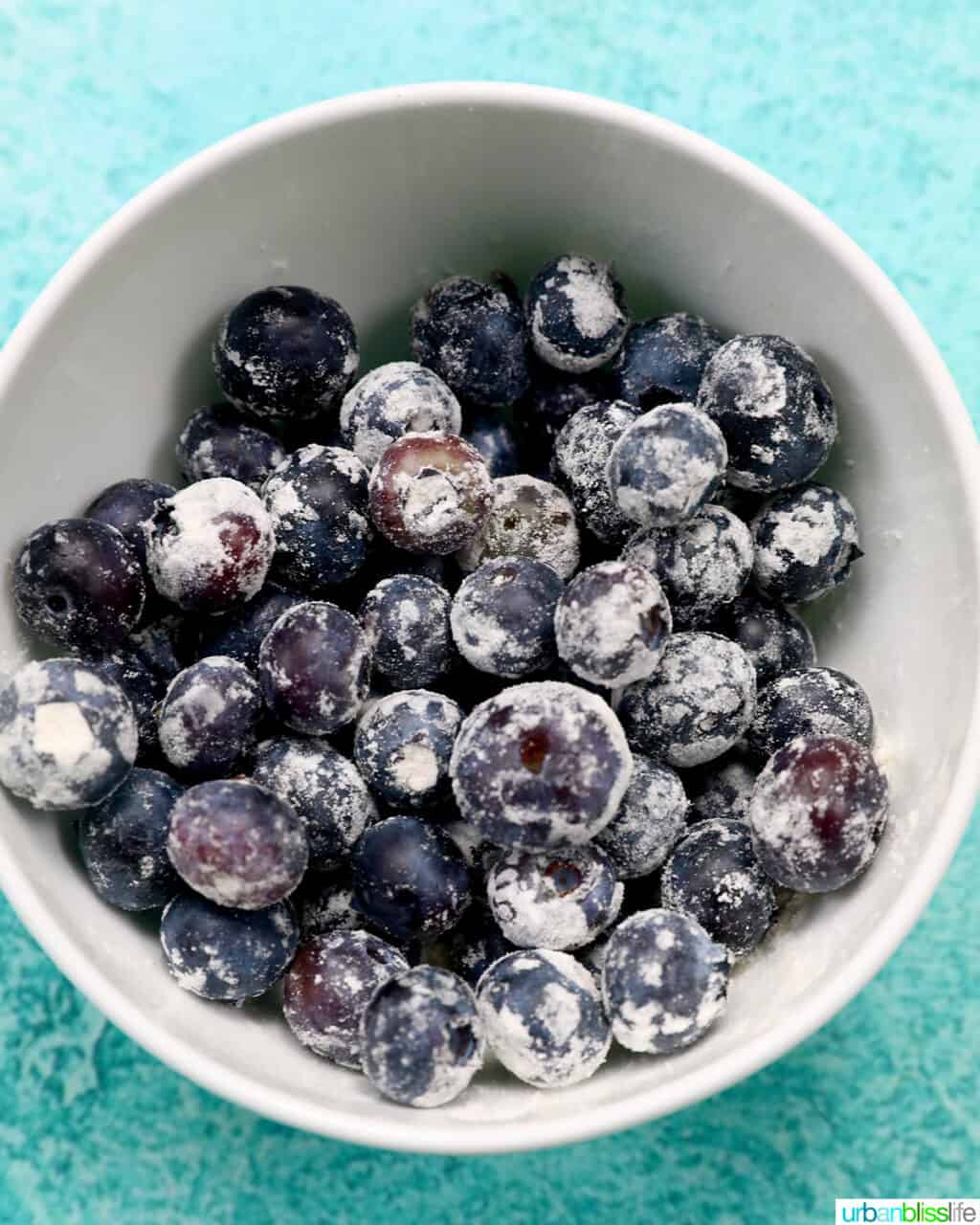 a white bowl full of floured blueberries.