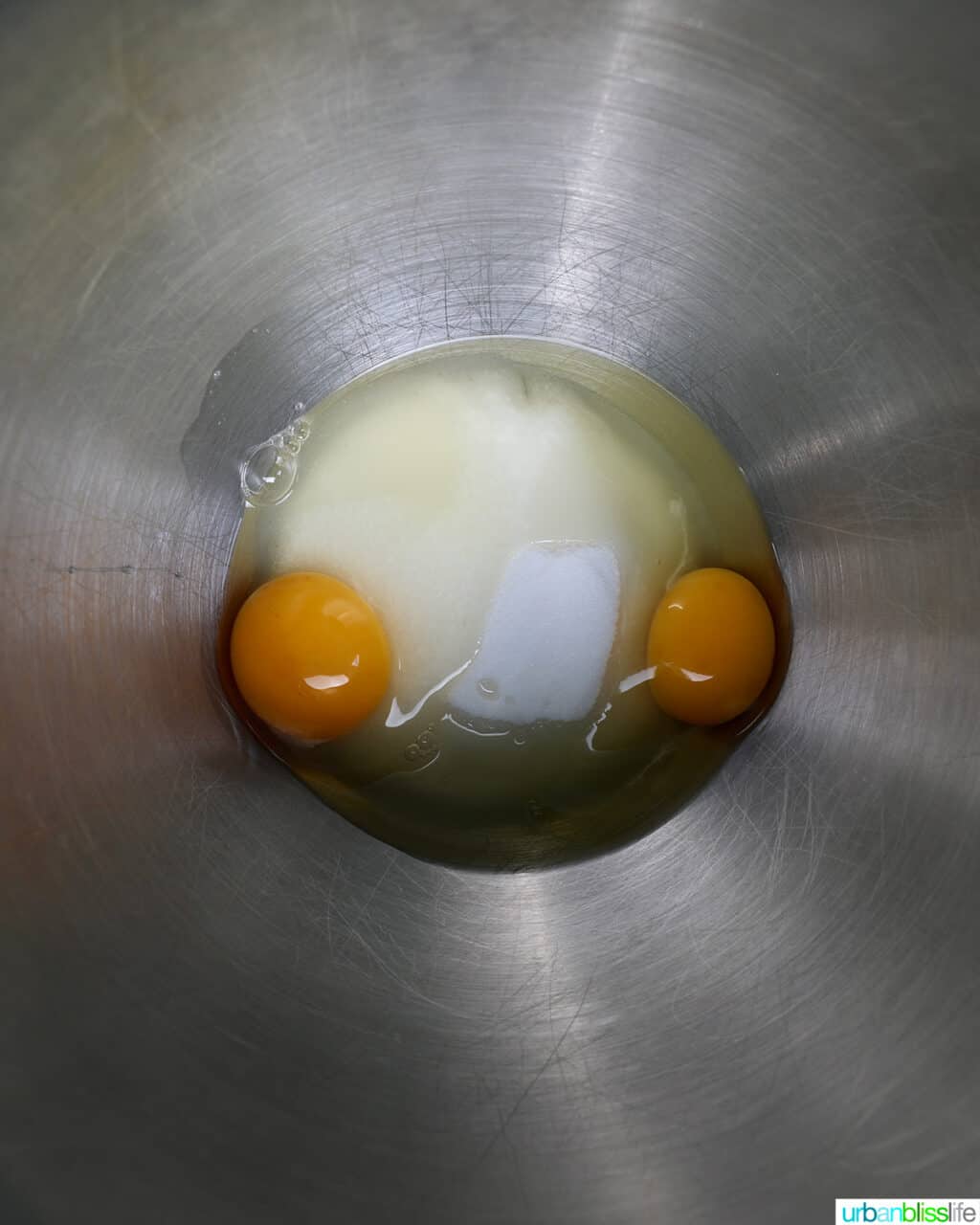 two eggs with sugar in a stainless steel bowl.