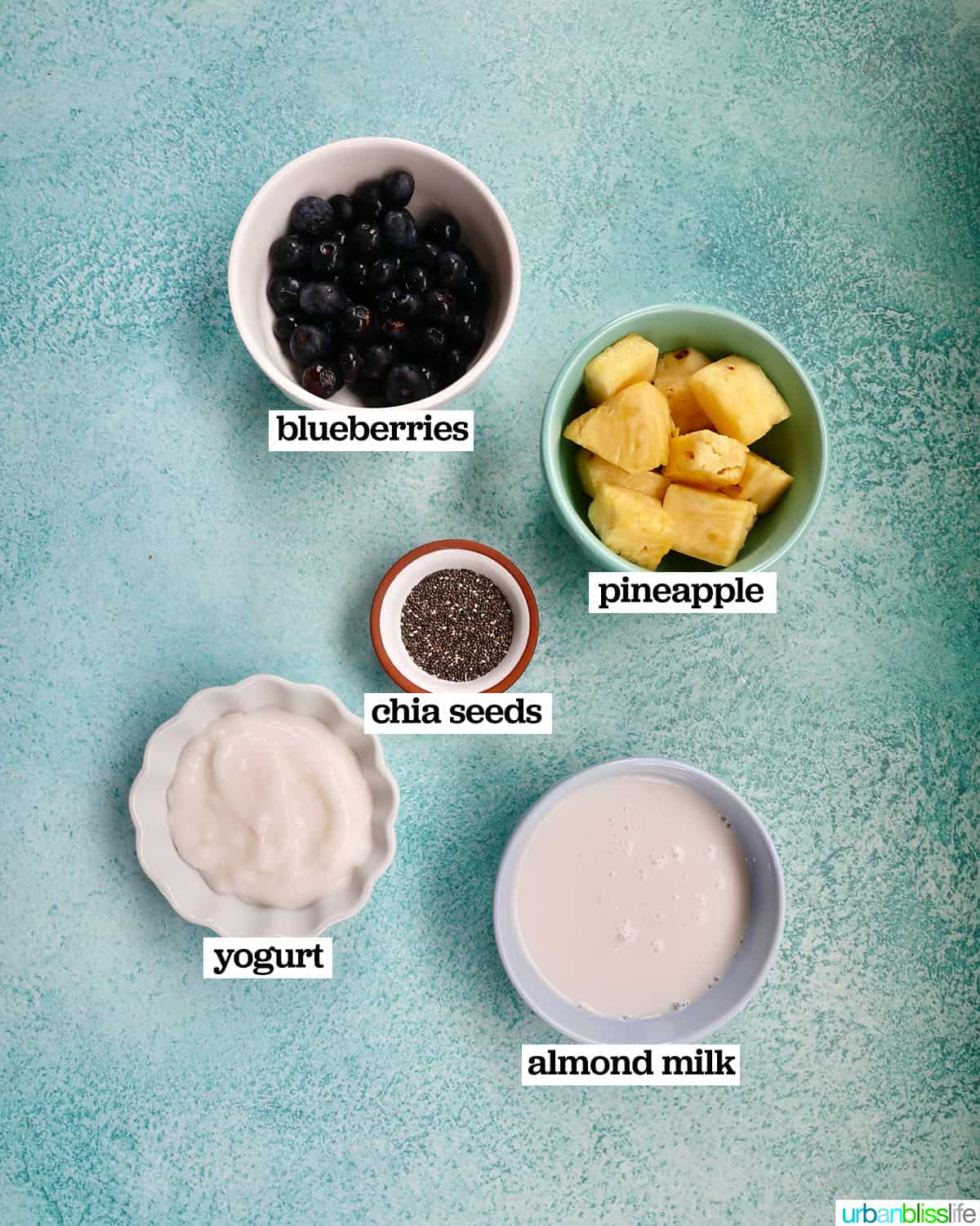 bowls of ingredients to make Blueberry Pineapple Smoothies on a bright blue table.