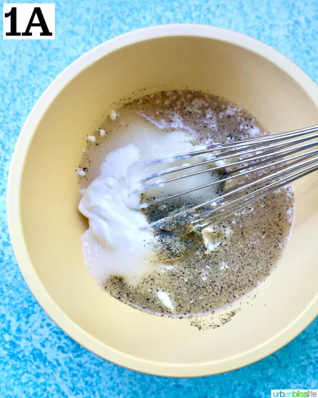 whisking ingredients to make salad dressing in a yellow bowl on top of a blue table.