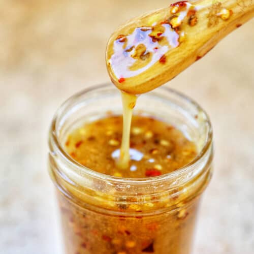 honey spoon lifting hot honey sauce out of a mason jar.