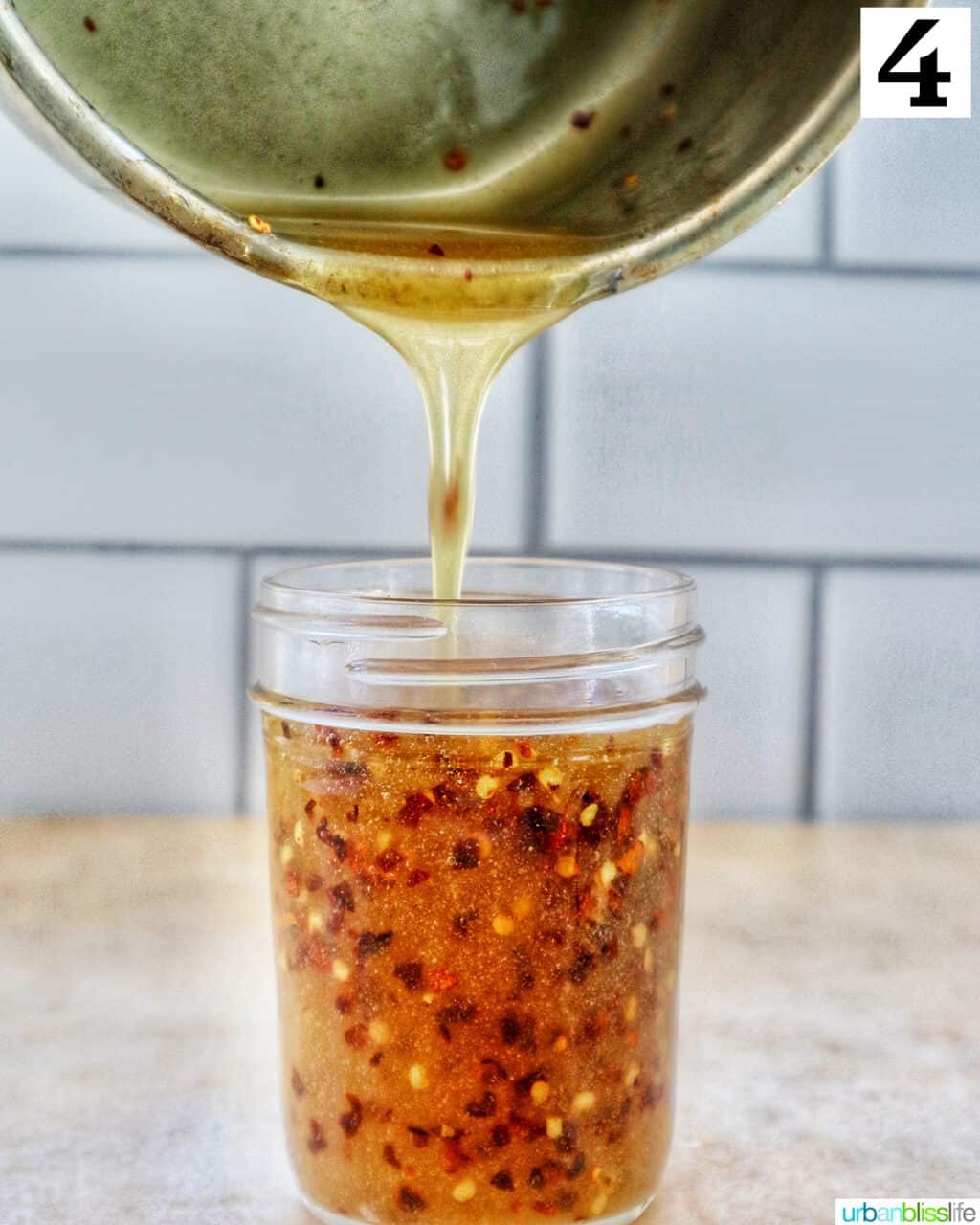 pouring hot honey sauce out of a saucepan and into a mason jar.