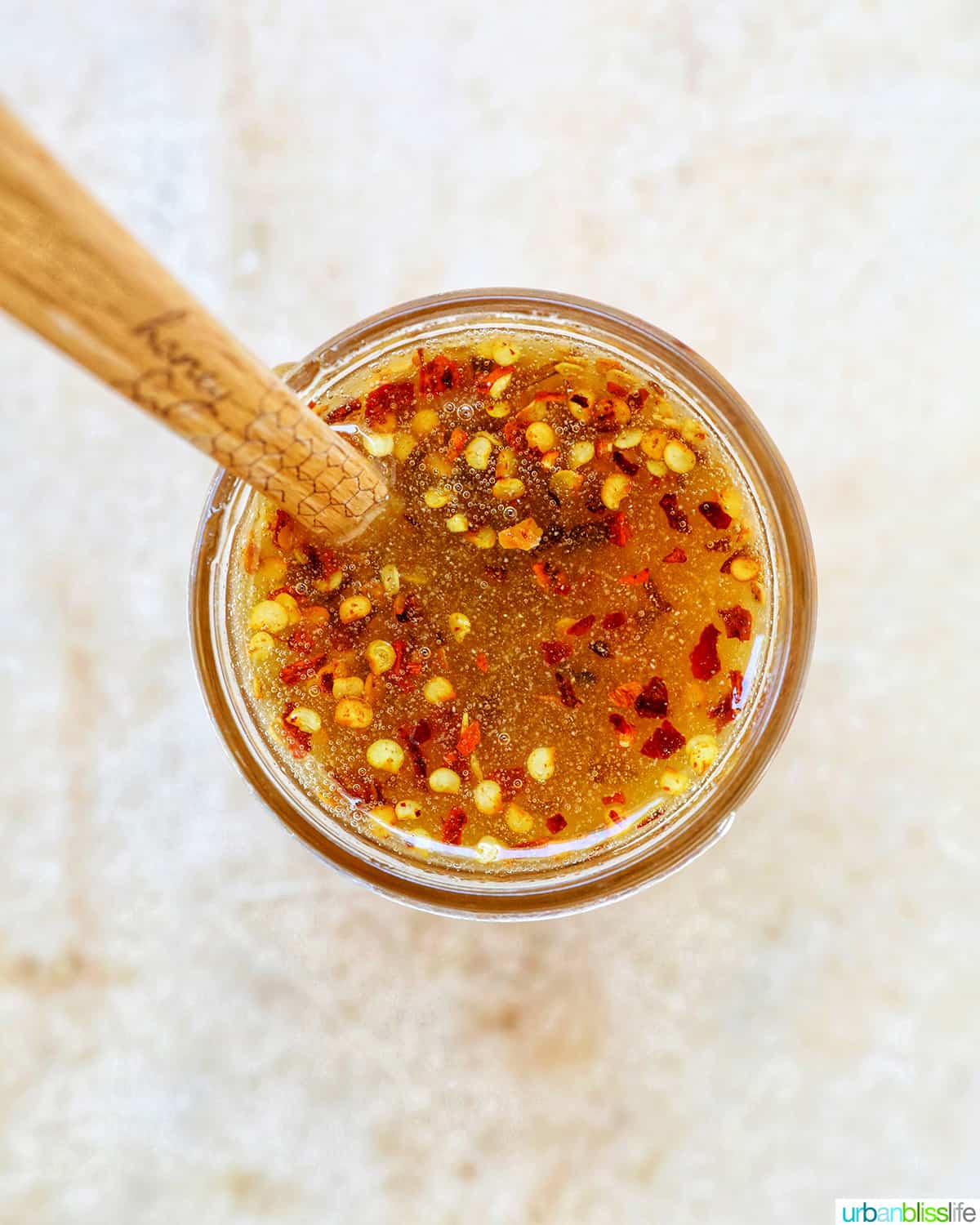 wooden spoon sticking out of the top of an opened jar of hot honey sauce.