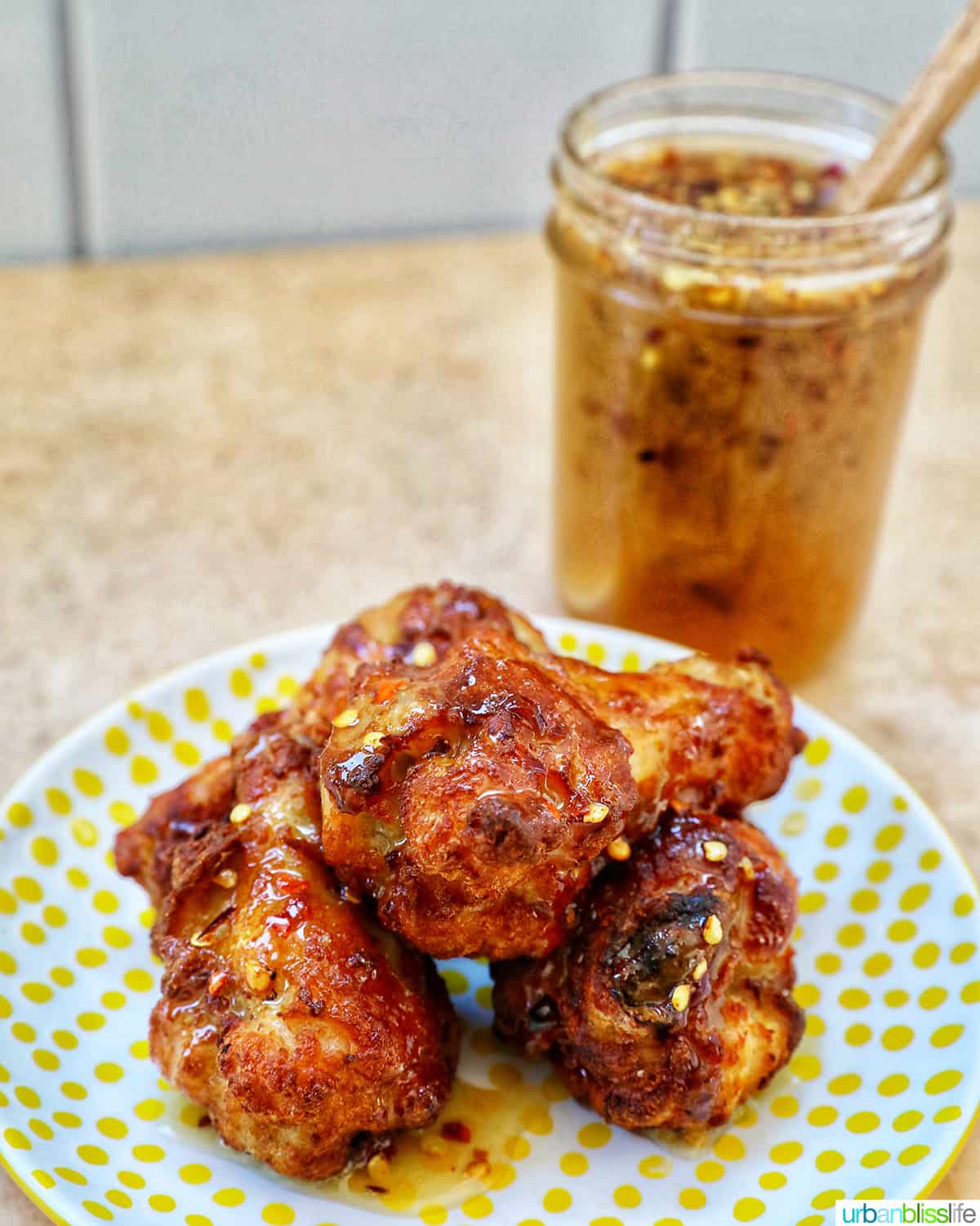 jar of hot honey sauce behind a plate full of hot honey chicken wings.